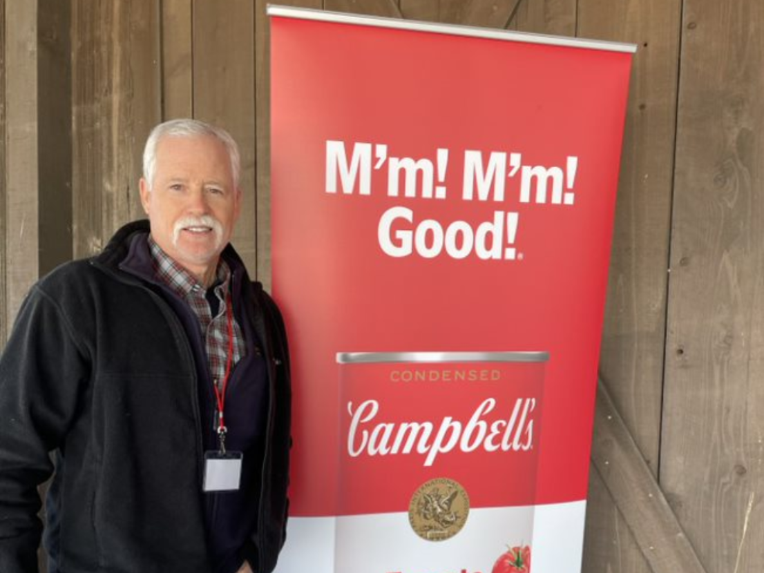 Bruce Rominger poses by Campbell's Tomato Soup sign